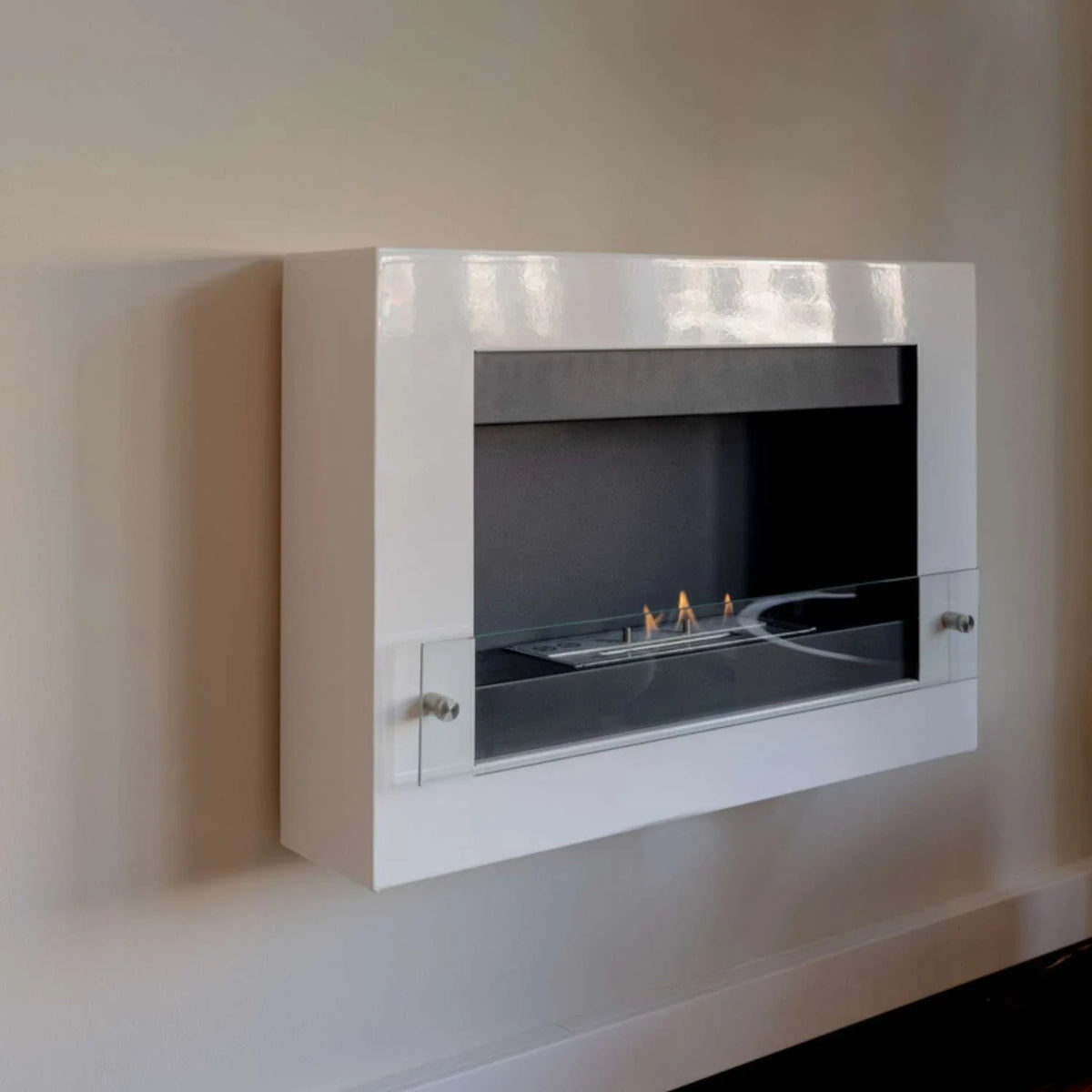 White wall-mounted bioethanol fireplace lit at an angle on a plain wall, close-up real-room view